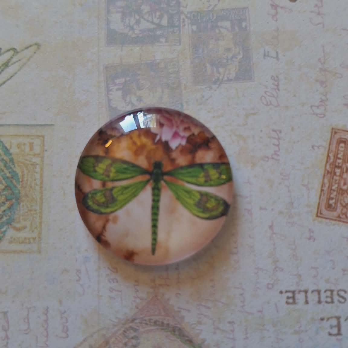 Round decorative item with a dragonfly design on a textured background with stamps and text.