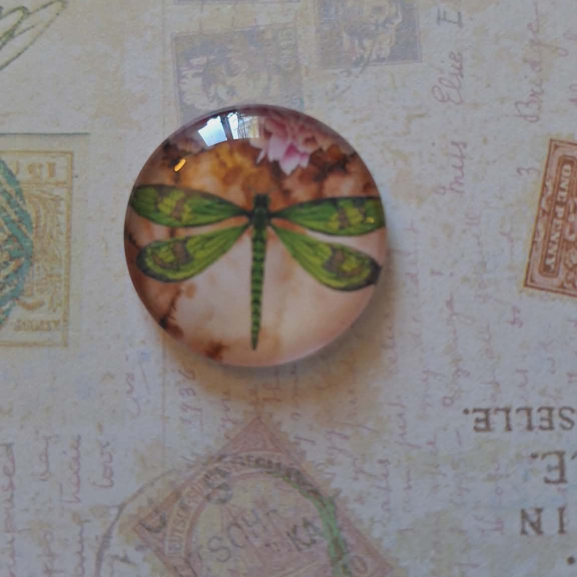 Round decorative item with a dragonfly design on a textured background with stamps and text.