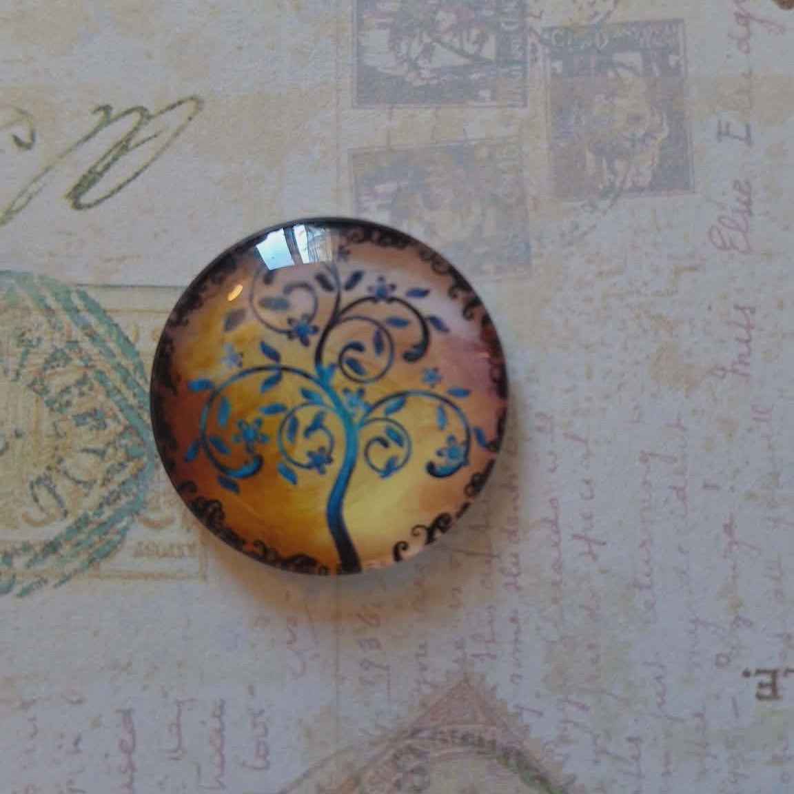 Decorative glass cabochon with tree design on an old letter background