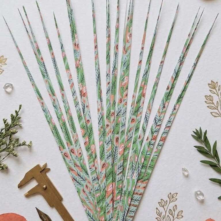 Decorative paper precut strips with floral pattern on a white background with greenery and pink leaves.