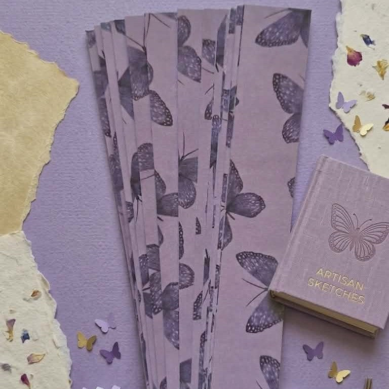 Butterfly-patterned paper and a small book on a textured purple surface.