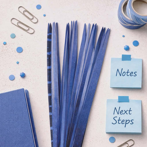 Blue stationery items including a notebook, ribbons, and sticky notes on a light background