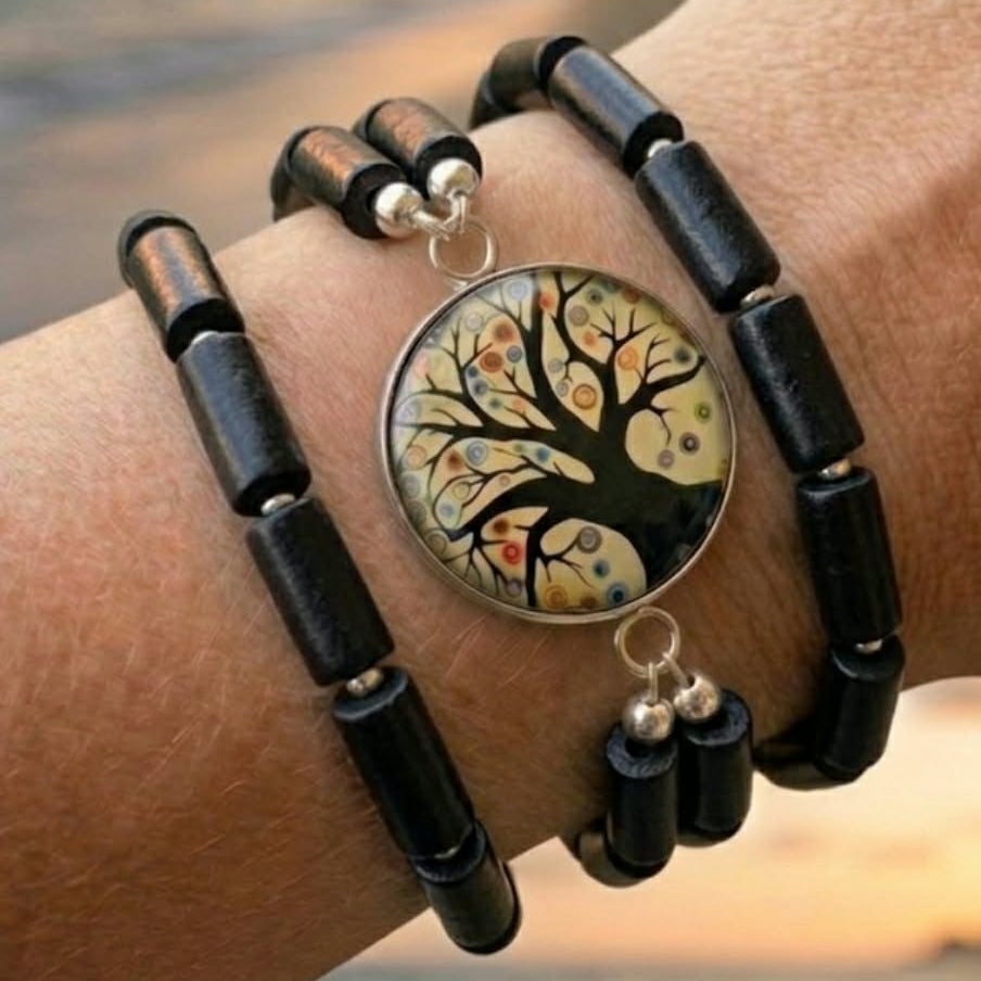 Black beaded bracelet with a tree of life design on a wrist against a blurred natural background