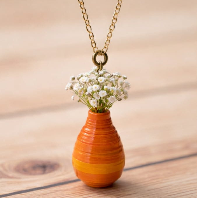 Necklace with a small orange vase pendant containing flowers on a wooden surface