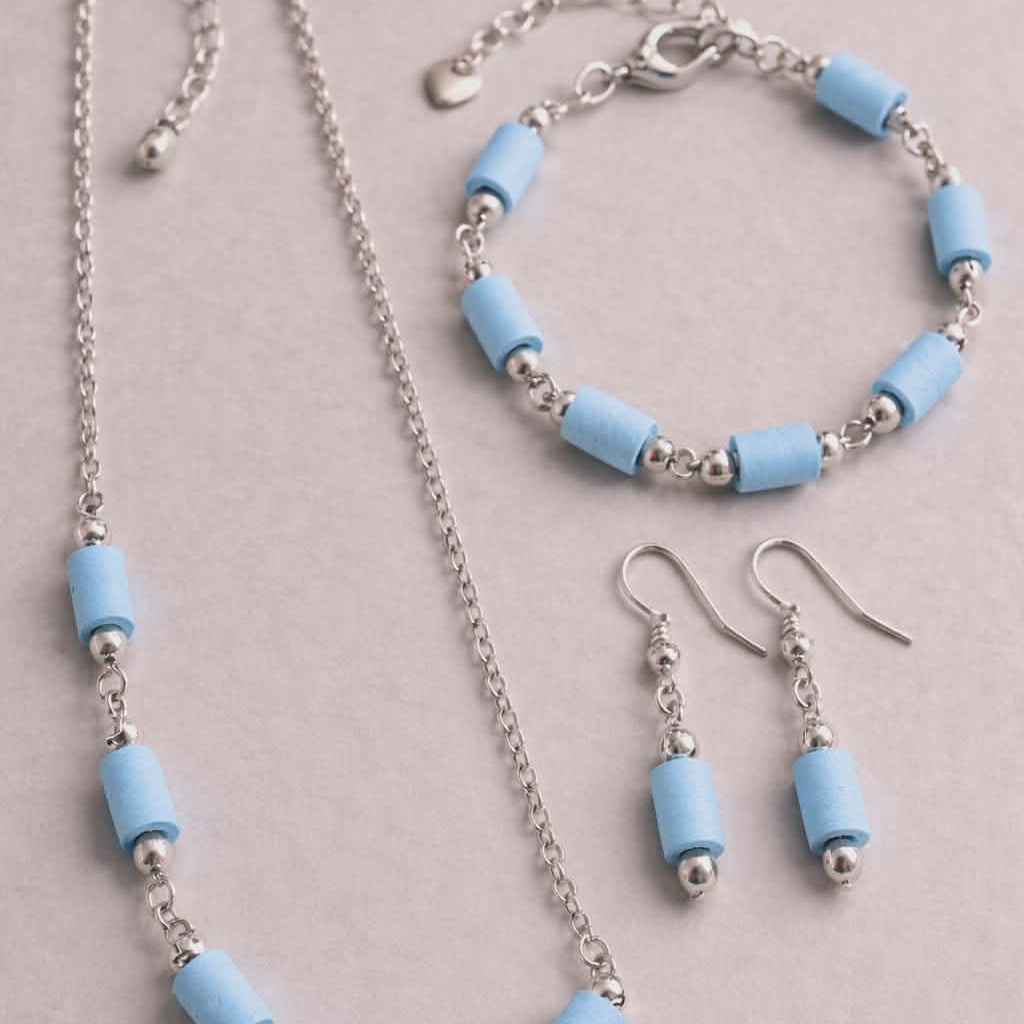 Jewelry set with necklace, bracelet, and earrings featuring light blue beads on a gray background