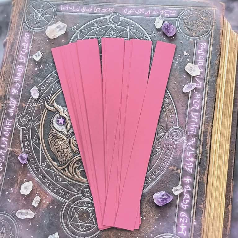 Light pink paper bead strips for rolling handmade paper beads, displayed on a decorative craft background with crystals.