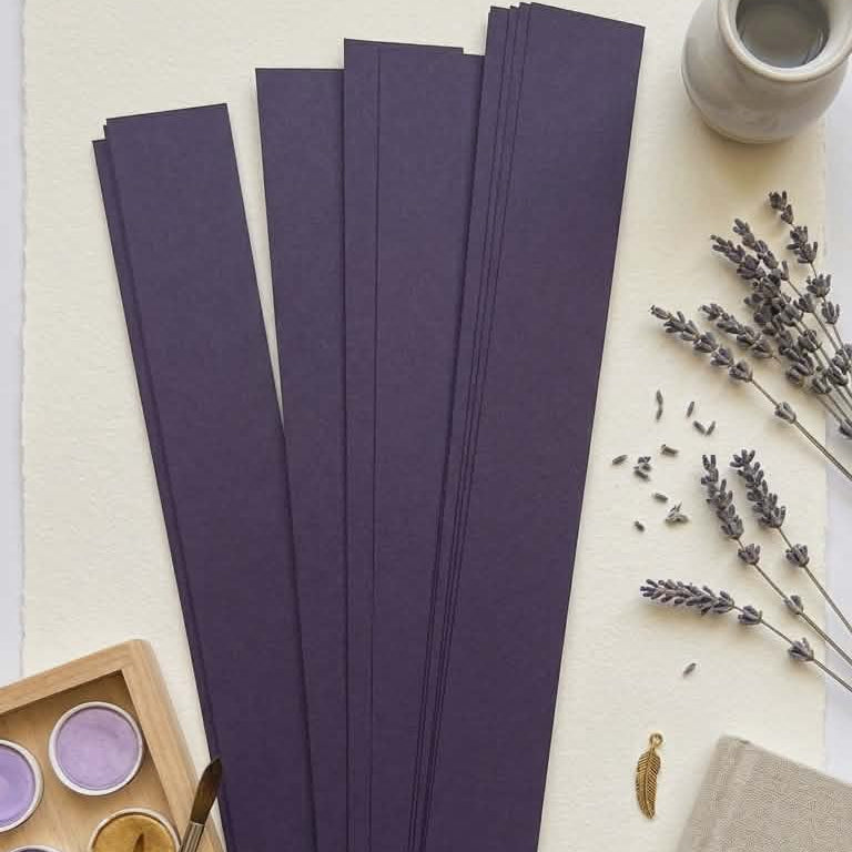 Purple paper strips with a watercolor palette, lavender flowers, and a notebook on a light surface.