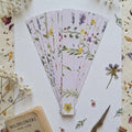 Set of floral-patterned pre-cut paper strips on a surface with dried flowers and a scissors.
