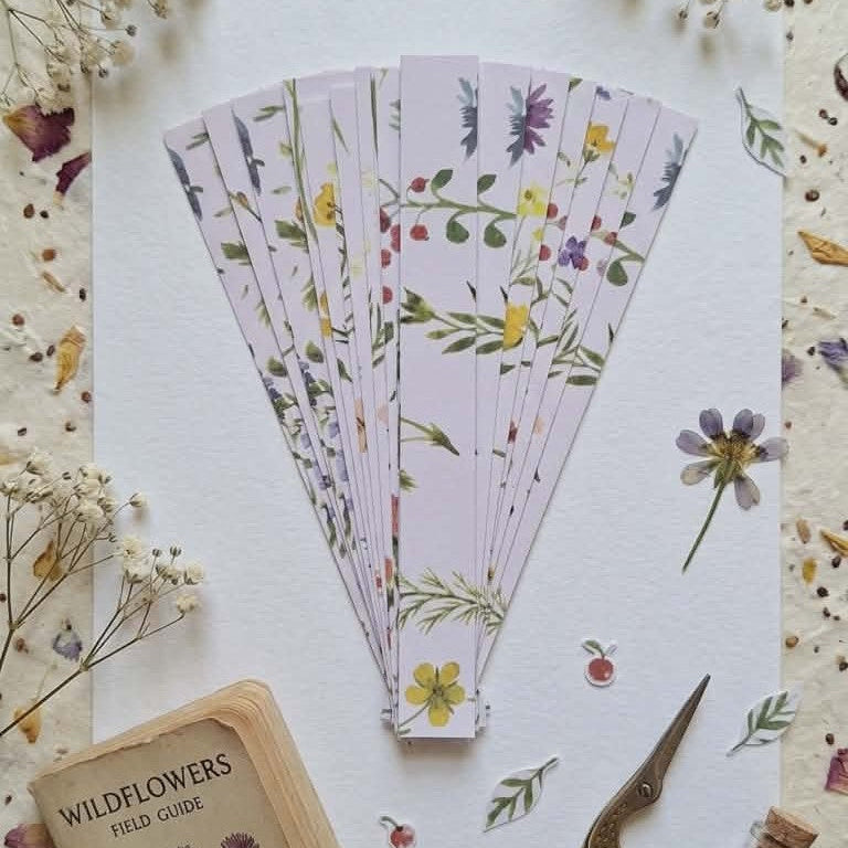 Set of floral-patterned pre-cut paper strips on a surface with dried flowers and a scissors.
